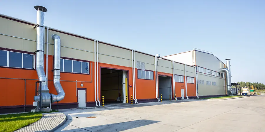 Industrie Großes Industriegebäude mit orange-beigem Äußeren, mehreren Garagentoren, Lüftungsrohren und einer gepflasterten Zufahrt unter freiem Himmel.