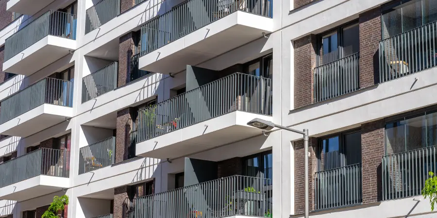 Wohnungswirtschaft Moderne Wohnhausfassade mit mehreren Balkonen mit Metallgeländern und Glastüren, von denen einige mit Pflanzen und Gartenmöbeln ausgestattet sind.